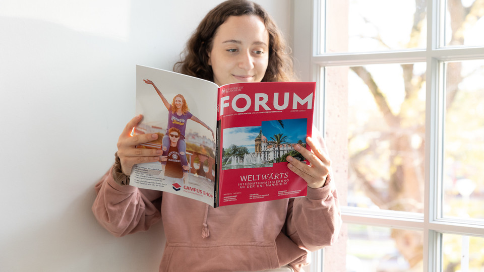 Eine Studentin lehnt an der Wand und liest das Magazin FORUM der Universität Mannheim.