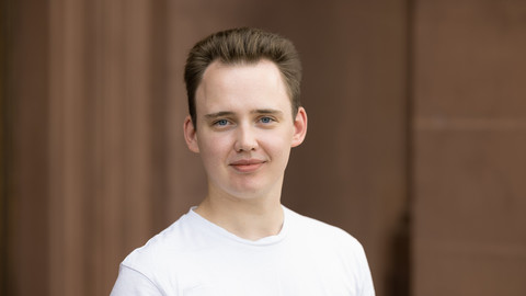 Domantas Undzėnas. He is wearing a white T-shirt and is standing in front of a stonewall.