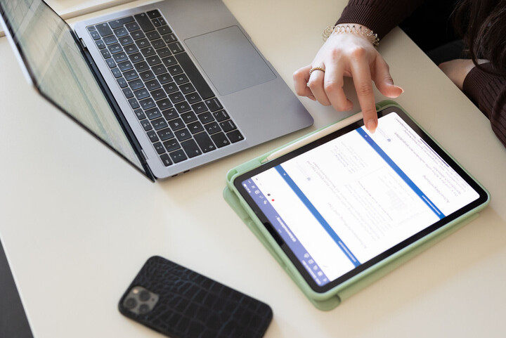 Eine Studentin tippt auf ihrem Tablet, ihr Handy und Laptop liegen daneben auf dem Tisch.