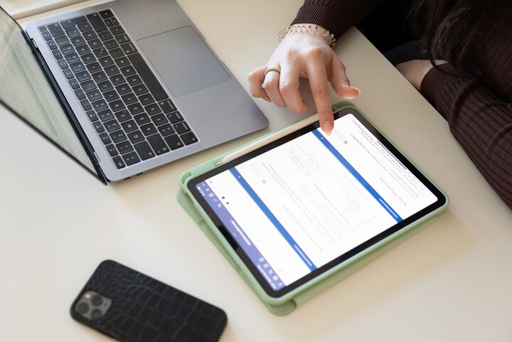 Eine Studentin tippt auf ihrem Tablet, ihr Handy und Laptop liegen daneben auf dem Tisch.