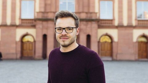 Paul Steger. He is wearing a black sweater and is standing on the Ehrenhof in front of the castle.