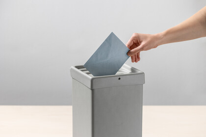 Eine Person steckt einen blauen Umschlag in eine Wahlurne.
