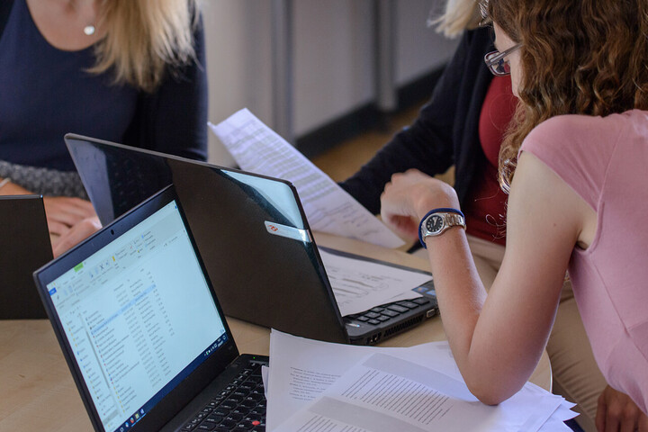 Drei Studentinnen sitzen mit ihren Laptops an einem Tisch und lernen gemeinsam.