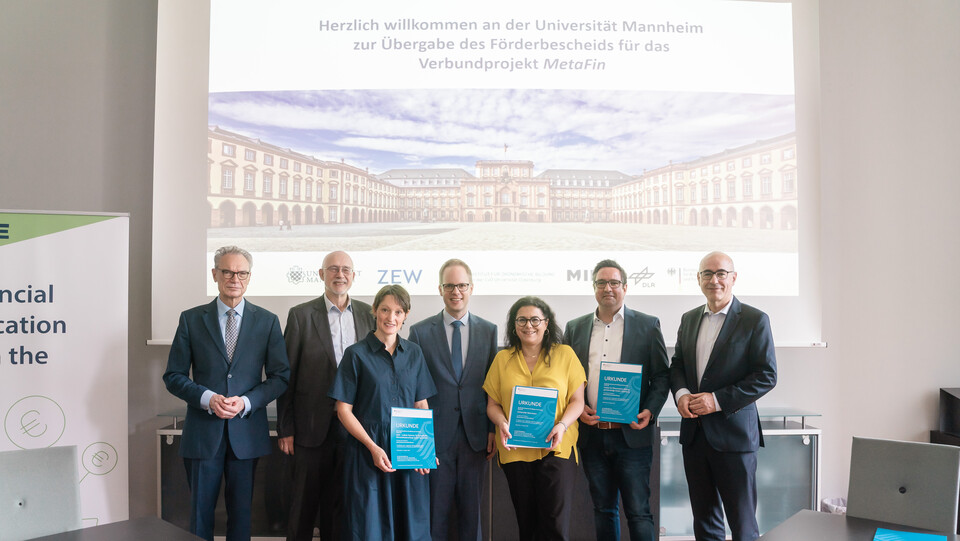 Die Projektleiter des MetaFin-Projekts stehen zusammen mit dem Rektor der Universität, dem Staatssekretär, dem Leiter des ZEW und dem Dekan der BWL-Fakultät im Senatssaal und präsentieren den Förderbescheid.