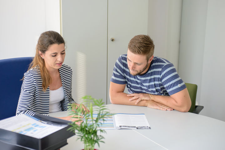 Mann und Frau schauen gemeinsam in ein Heft, der Mann wird beraten.