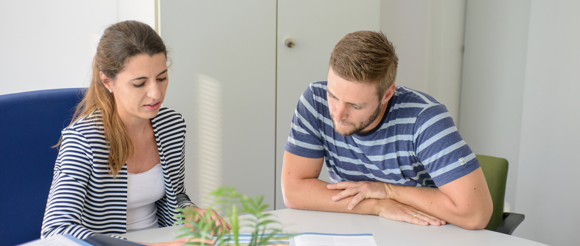 Mann und Frau schauen gemeinsam in ein Heft, der Mann wird beraten.