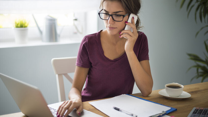 Having home office is a great solution Eine Frau arbeitet an einem Laptop und telefoniert nebenbei mit ihrem Handy.