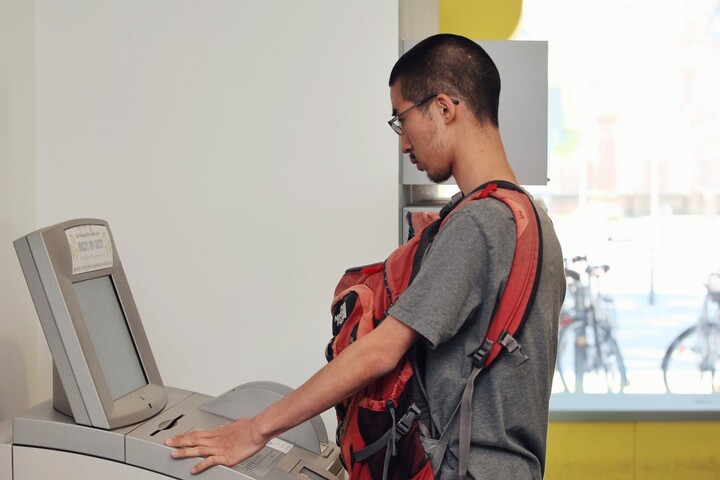 Ein Student steht an einem elektronischen SB-Terminal der Universität Mannheim. Er trägt einen roten Rucksack auf seinem Bauch.