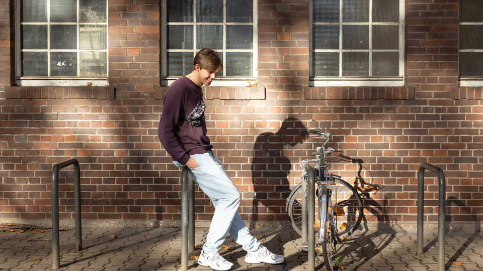 Ein sportlich gekleideter Student mit Bauchtasche lehnt an einem Fahrradständer