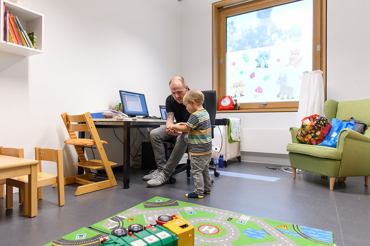 Vater und Sohn sitzen in einem Spielraum, der Vater zeigt dem Sohn etwas.
