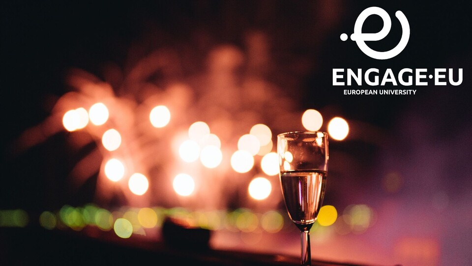 Ein Sektglas steht auf einer Mauer. Im Hintergrund ist ein Feuerwerk und rechts oben das Logo von Engage.EU.