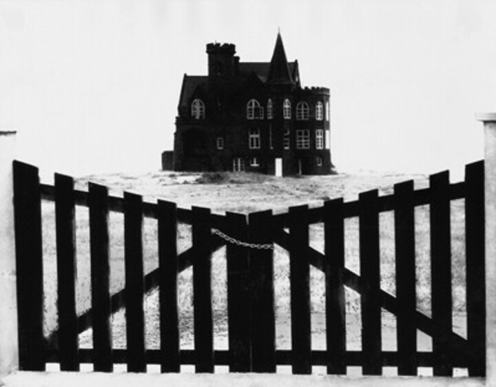 Schwarz-weiß-Bild eines Holztors mit einer Villa im Hintergrund.