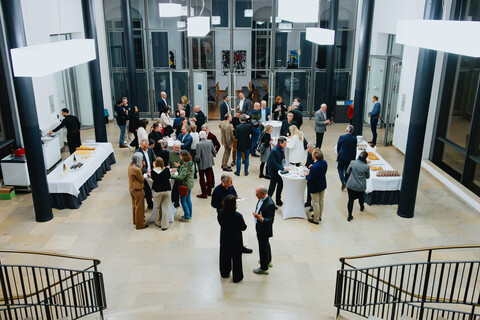 Das Bild zeigt aus einer erhöhten Position heraus eine Festgesellschaft zwischen Essens- und Getränkebuffet