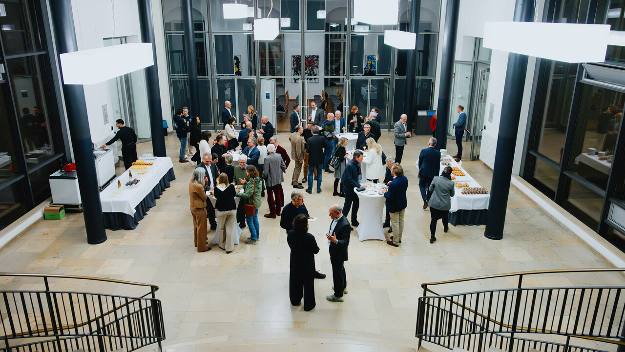 Das Bild zeigt aus einer erhöhten Position heraus eine Festgesellschaft zwischen Essens- und Getränkebuffet