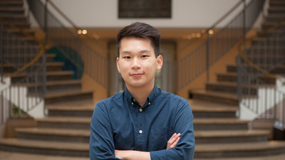 Eine Person trägt ein blaues Hemd und steht in einem Gebäude vor einer Treppe. Die Person heißt Hieu Nguyen.