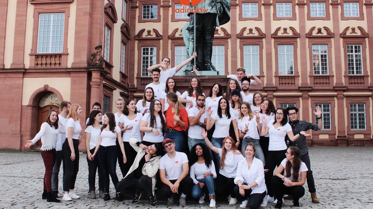 Studierende des Campusradios "Radioaktiv" posieren vor dem Mannheimer Schloss. Sie tragen weiße T-Shirts.