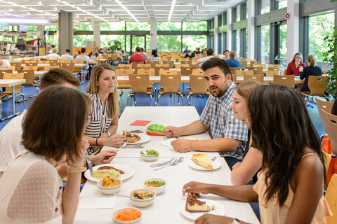 Studierende sitzen gemeinsam in der Mensa an einem Tisch und essen zu Mittag.