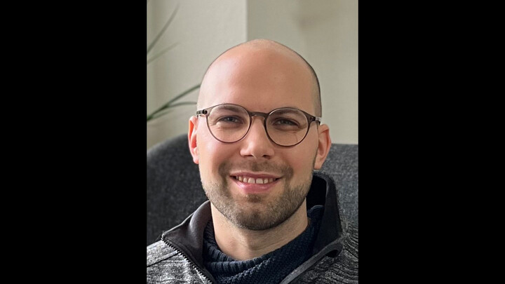 Portraitfoto von Dr. David Kretschmer. Er trägt einen weiß-grau gemusterten Pullover.