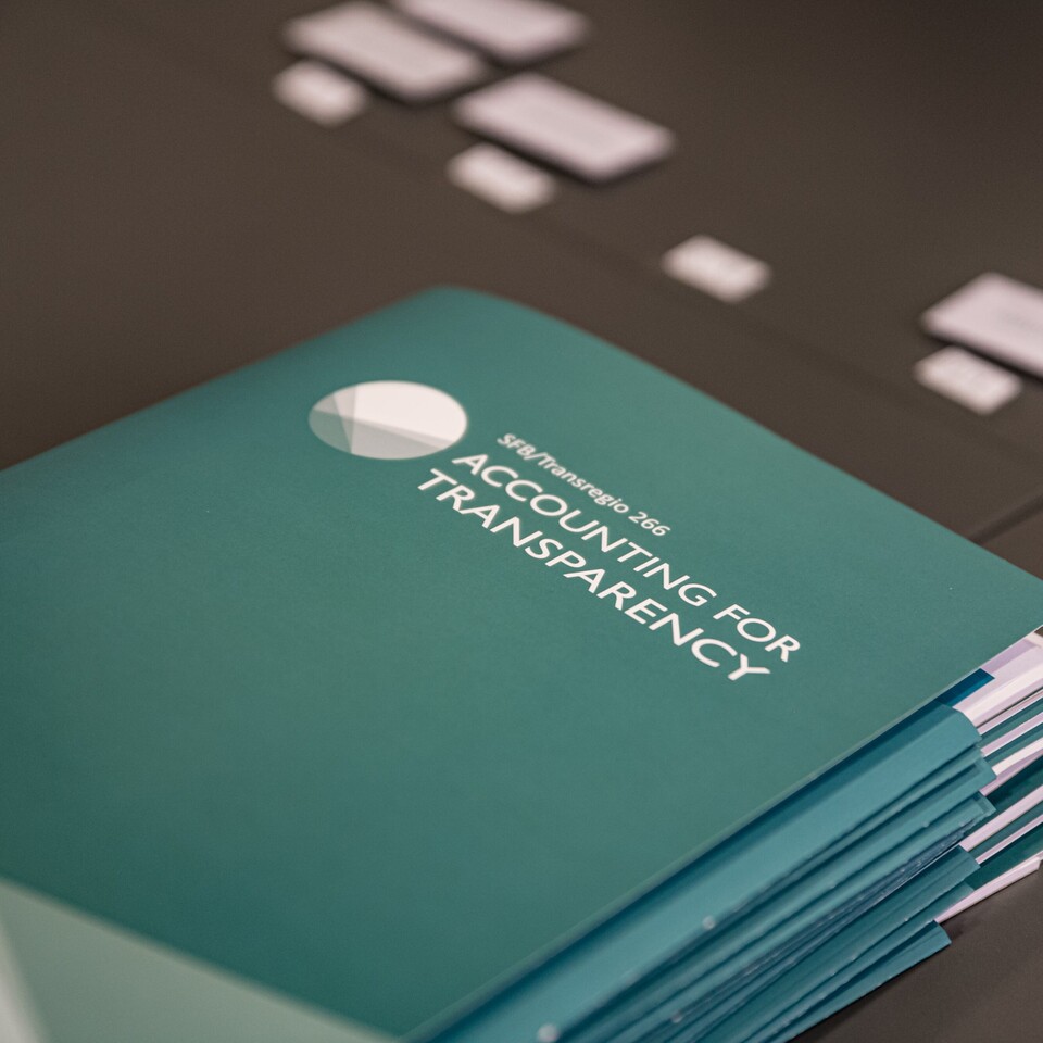 Türkisfarbene Mappen liegen auf einem schwarzen Tisch. Die Mappe haben die weiße Aufschrift "SFB/Transregio 266, Accounting for Transparency".