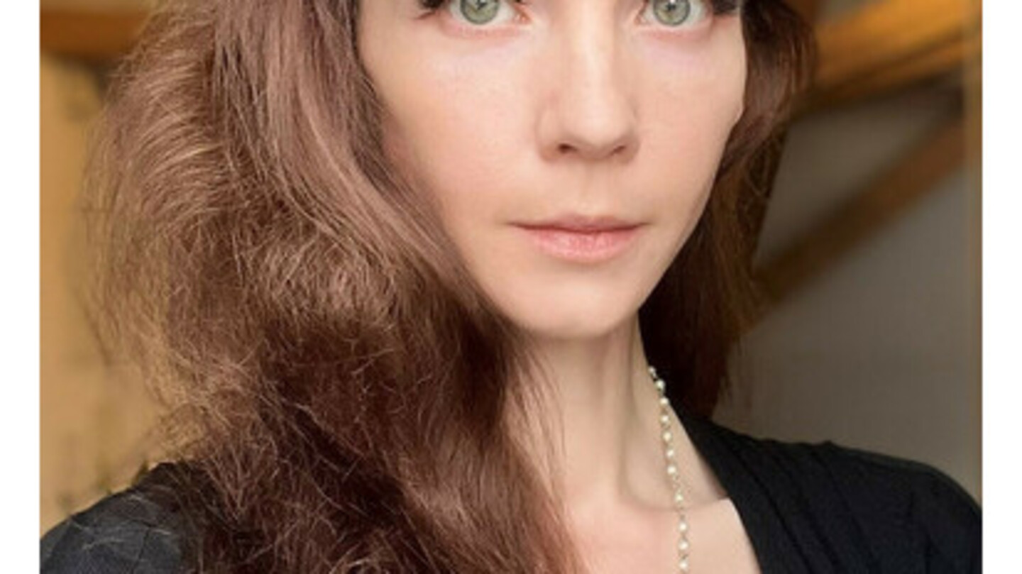 Iuliia Shkrabaliuk hat braune, gewellte lange Haare. Sie trägt ein schwarzes Jacket.