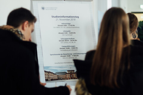 Studierende blicken auf das Programmplakat des Studieninfotags