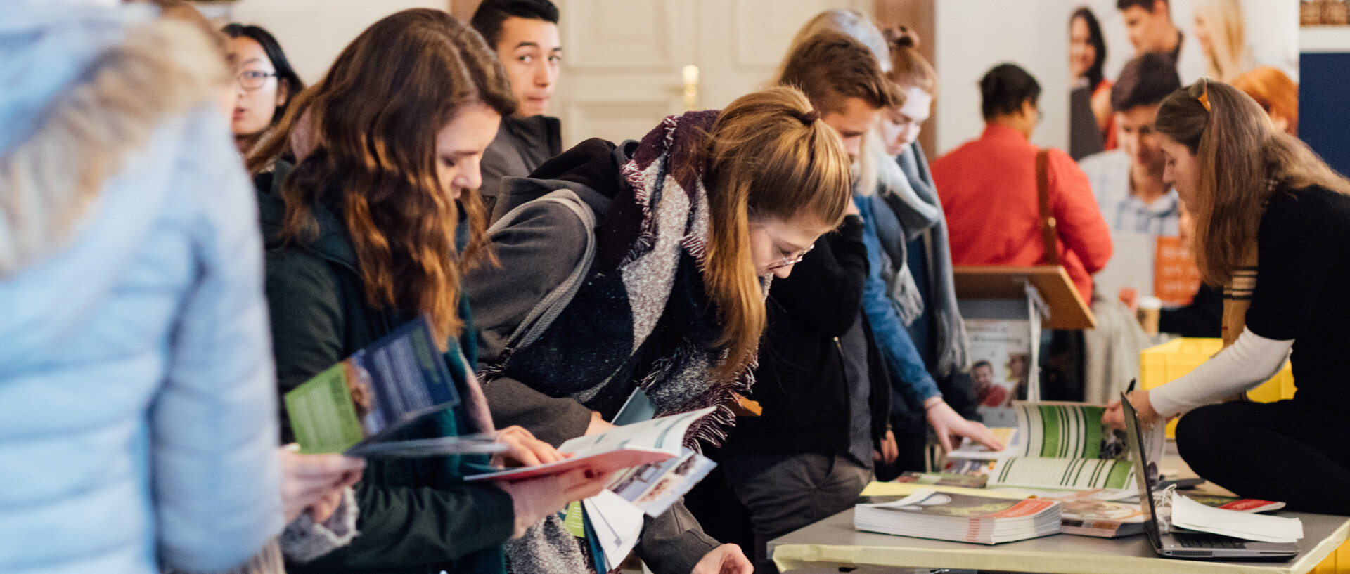 Mehrere Studieninteressierte, die beim Studieninfotag das Informationsmaterial auf Tischen sichten