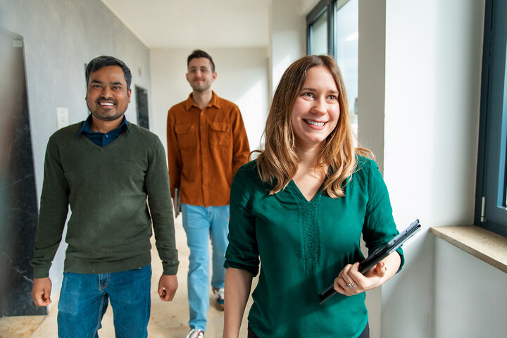 Three employees of the University of Mannheim walk through a corridor in a good mood