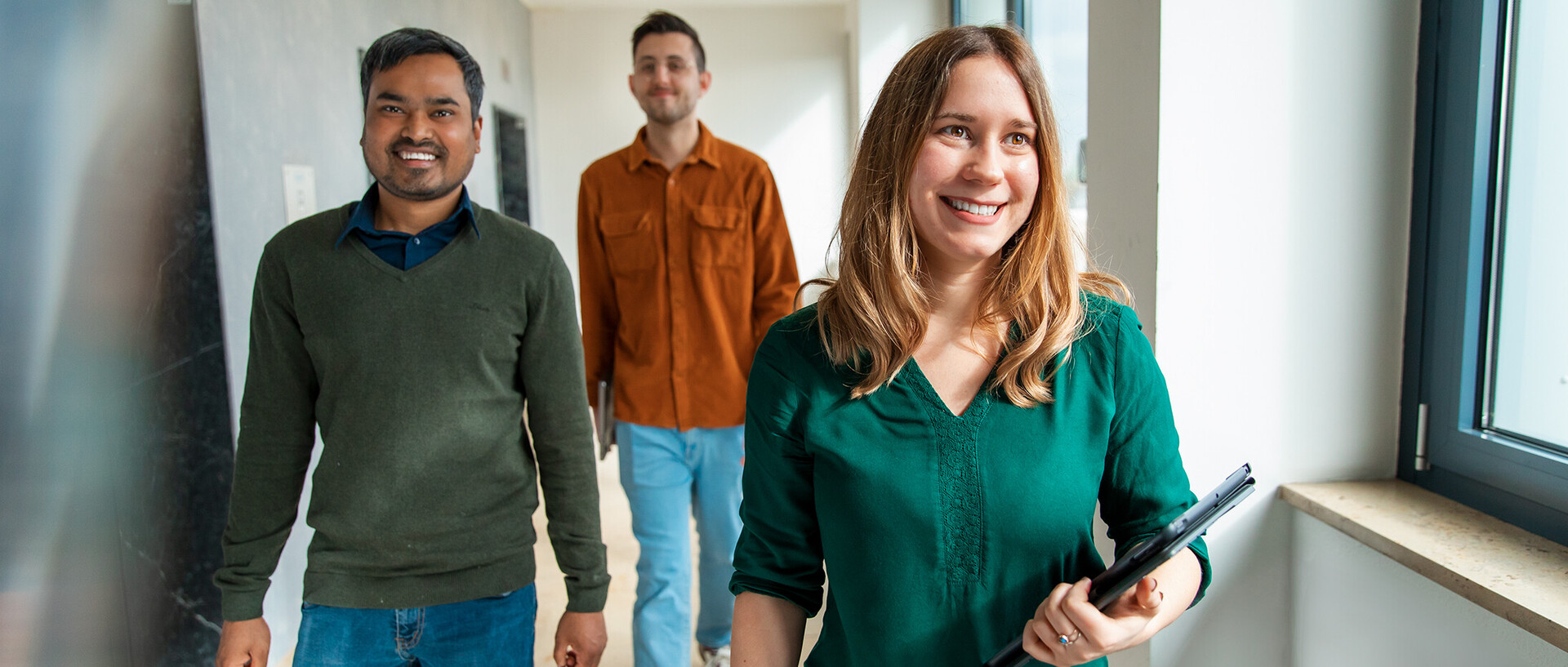 Three employees of the University of Mannheim walk through a corridor in a good mood