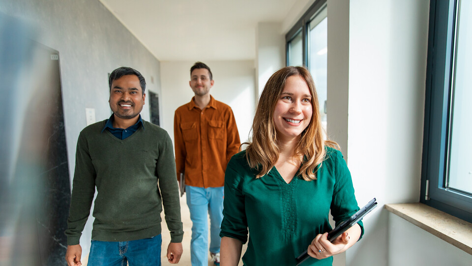 Three employees of the University of Mannheim walk through a corridor in a good mood