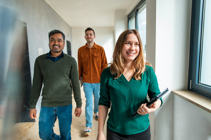 Three employees of the University of Mannheim walk through a corridor in a good mood