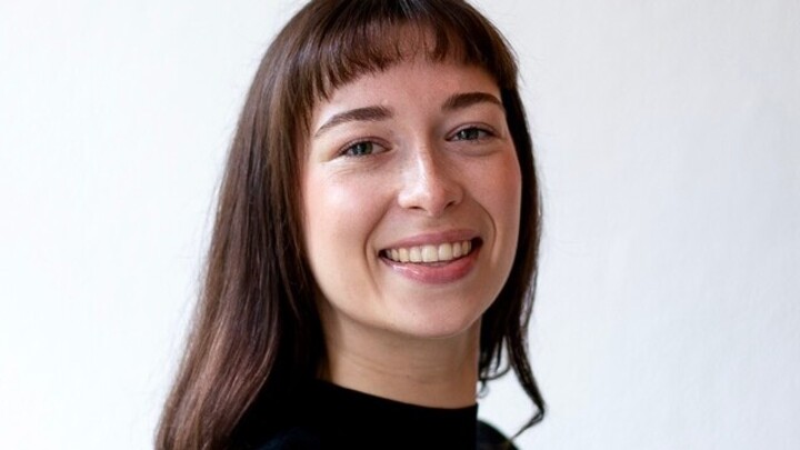 Portrait of Isabel Porstein. She is wearing a black shirt and standing in front of a white wall.