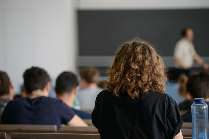 Studierende sitzen hintereinander in einem Hörsaal und hören bei einer Vorlesung zu.