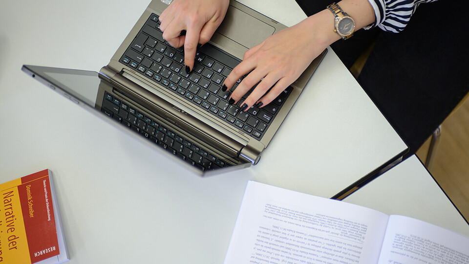Zwei Hände einer Frau tippen auf der Tastatur eines Laptops.