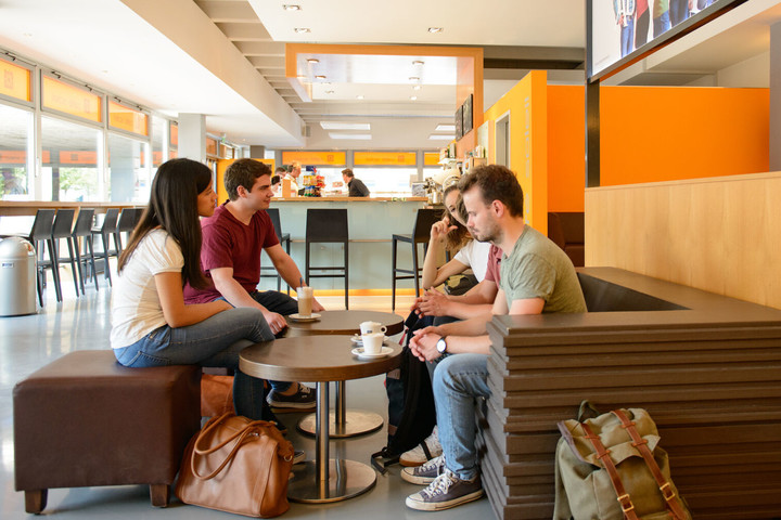 Eine Gruppe von Studierenden sitzt um einen Café-Tisch in der Mensa.