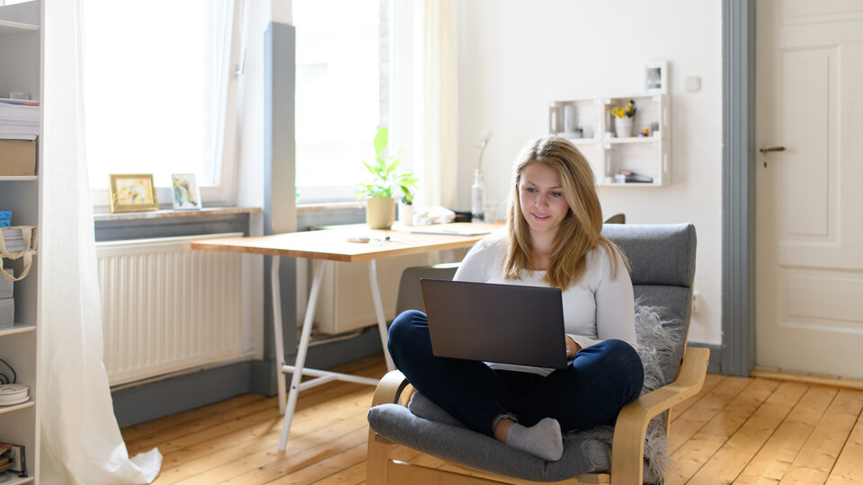 Studentin mit blonden Haaren sitzt zu Hause am Laptop