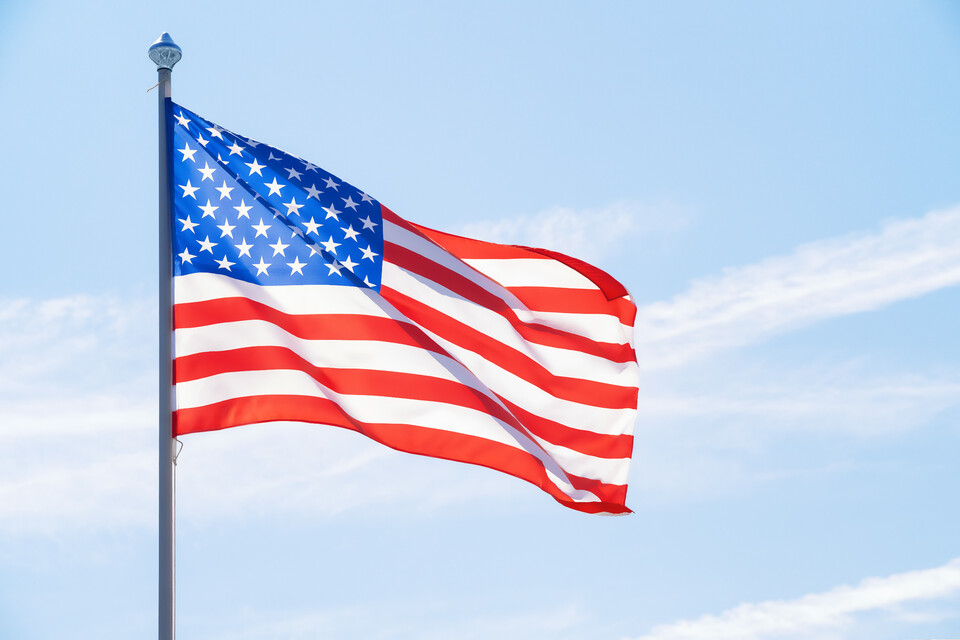 Amerikanische Flagge weht im Wind. Im Hintergrund ein blauer Himmel mit Wolkenstreifen.