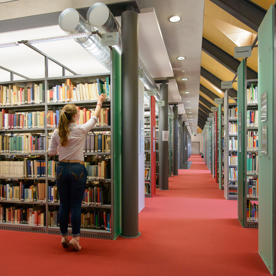 Eine Studentin nimmt ein Buch aus einem Regal voller Bücher.