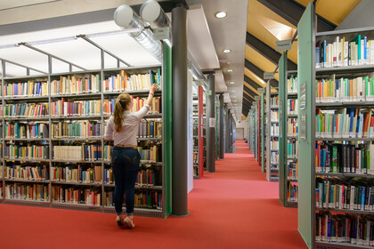 Eine Studentin nimmt ein Buch aus einem Regal voller Bücher.