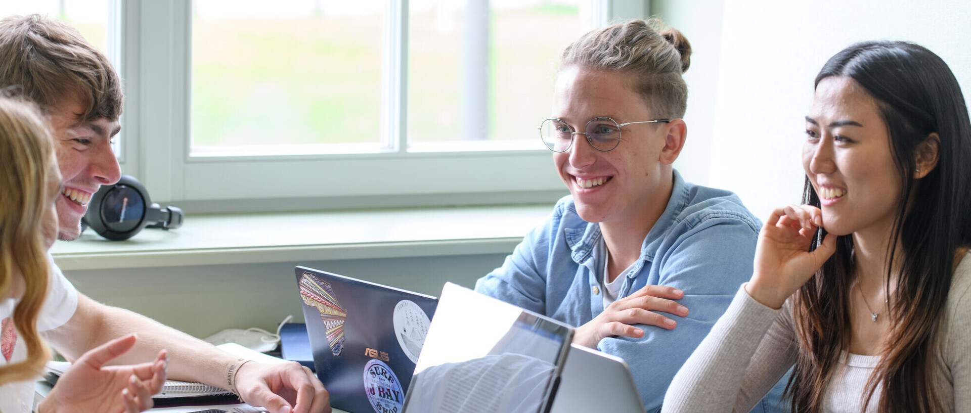 Vier lachende Studierende, die zusammen vor ihren Laptops am Tisch sitzen