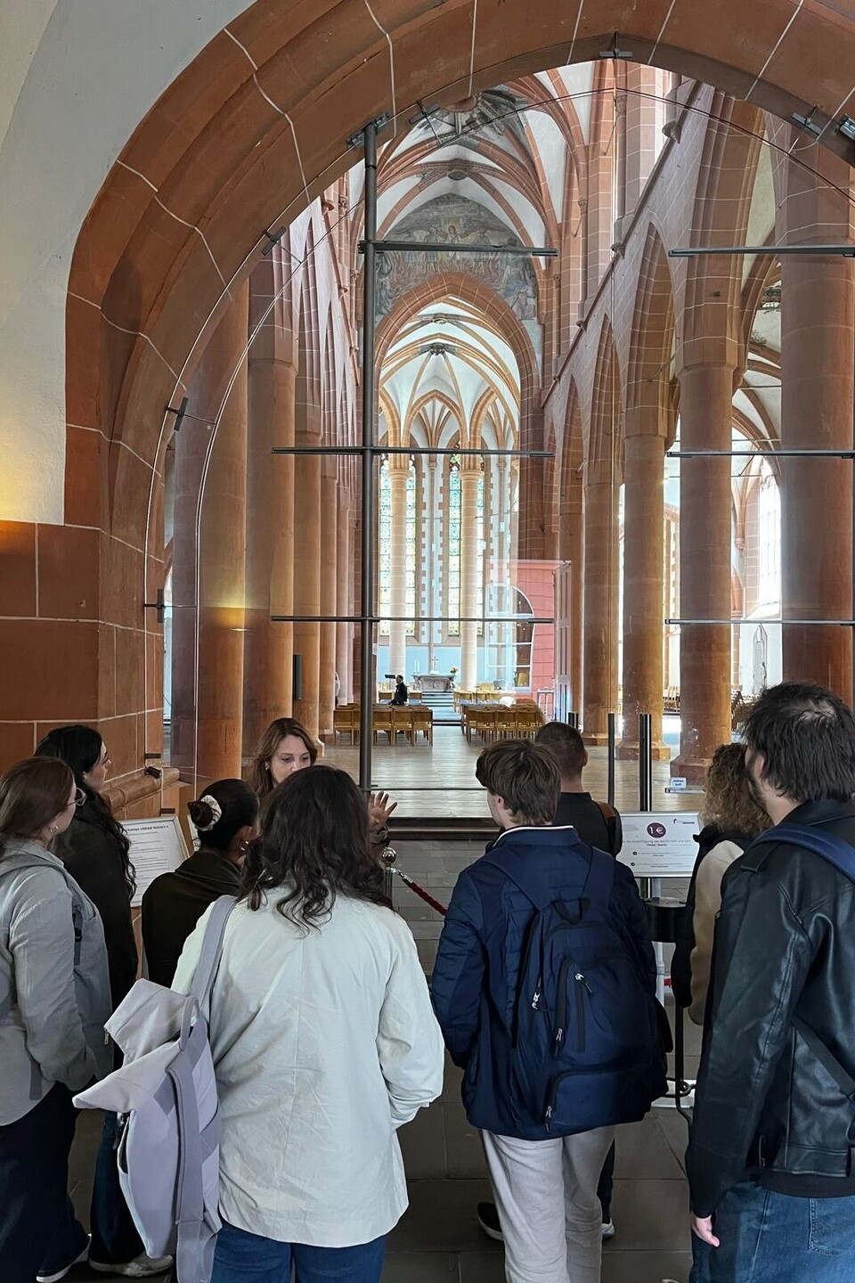 Eine Gruppe von Personen im Eingang der gotischen Heidelberger Stiftskirche, die einer anderen Person zuhören.
