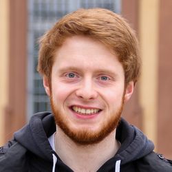 Tobias Kahlenberg hat kurzes rot- orangenes Haar sowie einen Bart in der selben Farbe. Er hat blaue Augen und lächelt. Er trägt einen schwarzen Kapuzenpulli und eine schwarze Jacke darüber.