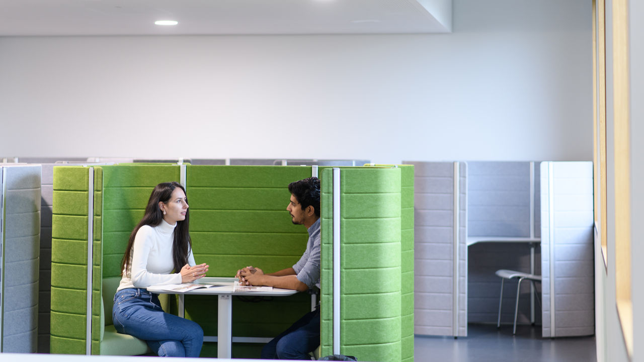 Eine Studentin und ein Student sitzen in einem abgetrennten grünen Arbeitsbereich.
