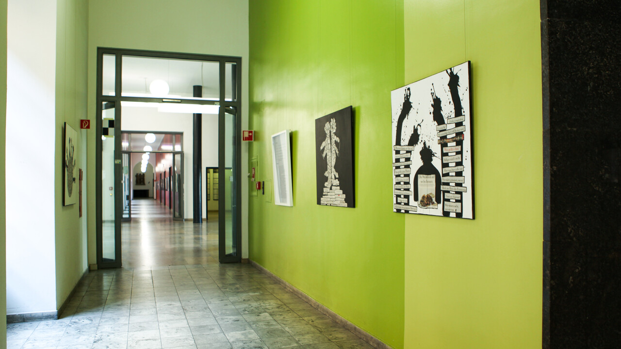 In einem Flur hängen Kunstwerke, die aus Zeitungscollagen und Abbildungen von schwarzen Farbklecks-Figuren bestehen.