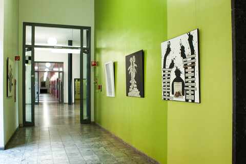 In einem Flur hängen Kunstwerke, die aus Zeitungscollagen und Abbildungen von schwarzen Farbklecks-Figuren bestehen.