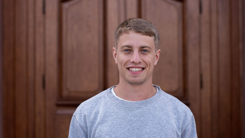 Paul Wegener. He is wearing a grey sweater and is standing in front of a brown door.