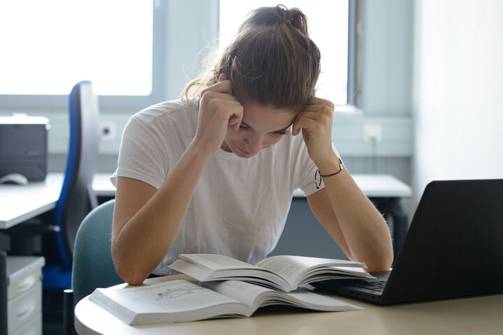 A student holds her head and reads a book