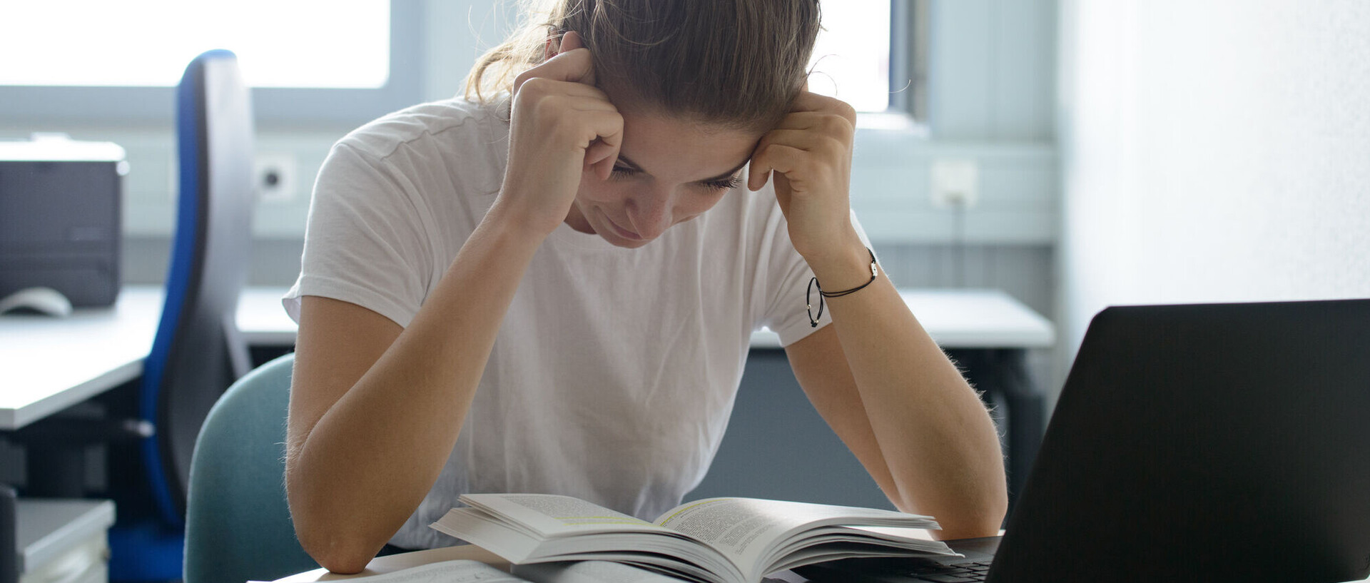 A student holds her head and reads a book