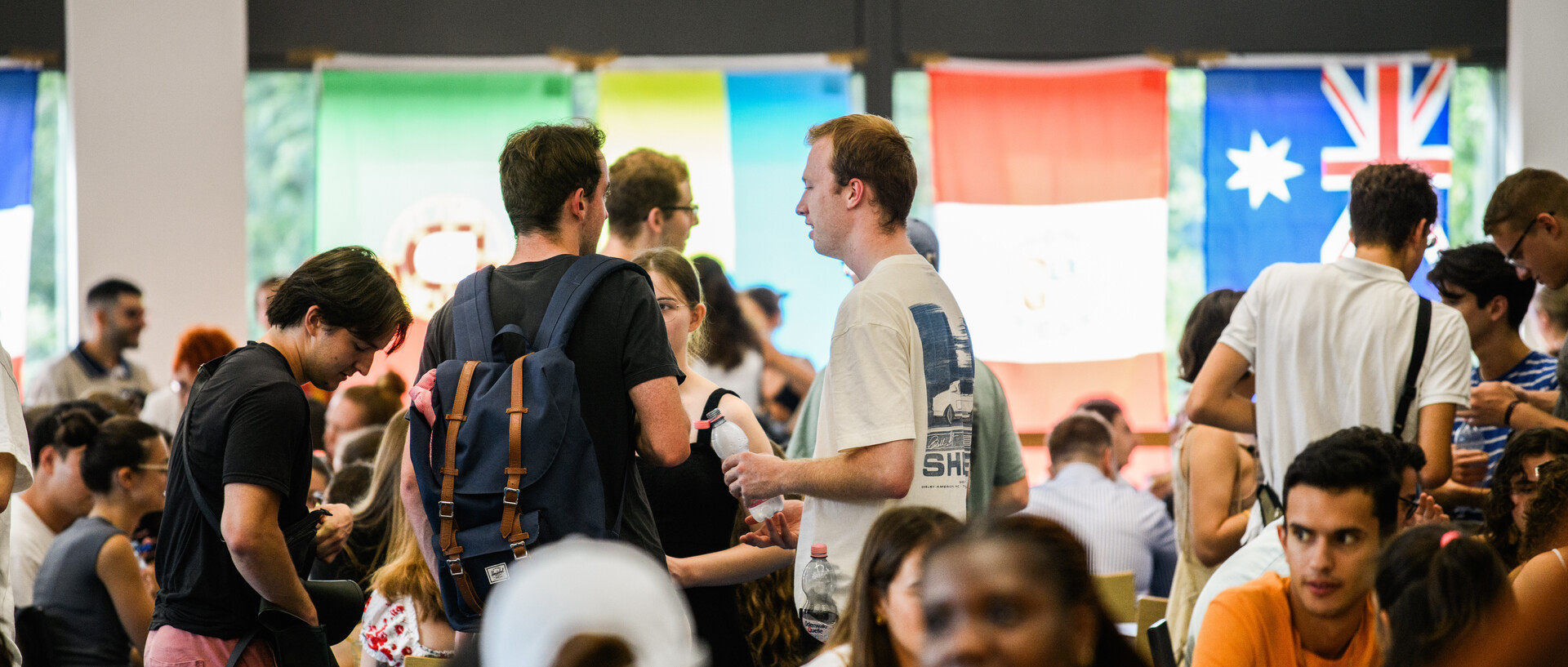 Students sit and stand in the Mensa and talk.