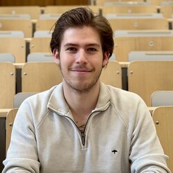 Porträt von Luca Zeitler. Luca Zeitler trägt einen beigen Pullover und einen dezenten Vollbart. Die dunkelblonden Haare hat sind etwas länger und nach hinten gekämmt. Luca Zeitler lächelt offen in die Kamera. 