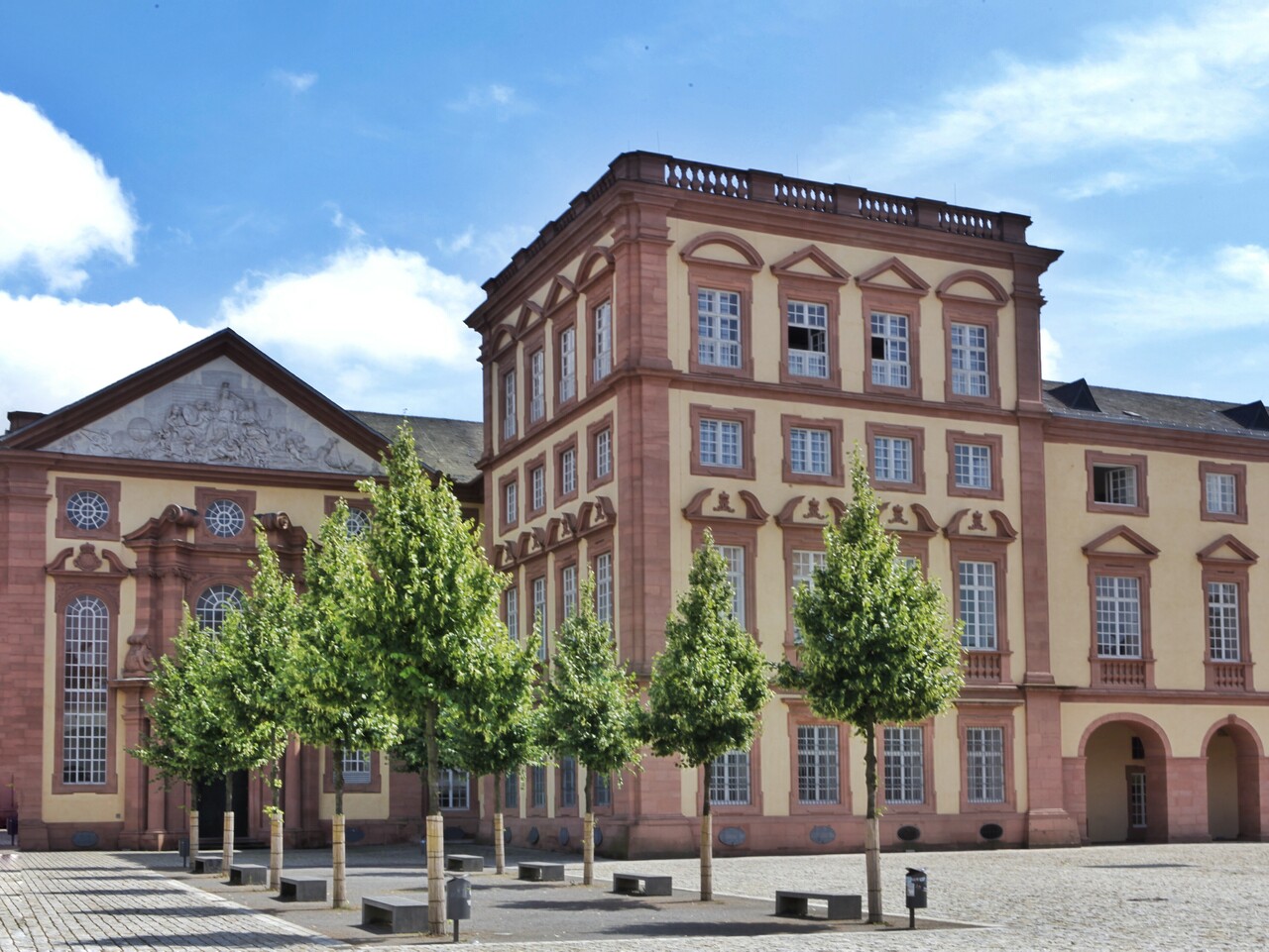 Schloss Mannheim Der Kunstturm und der Ehrenhof Ost im Sonnenlicht. Davor grün belaubte Bäume.